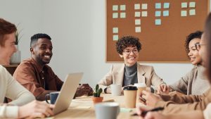 Diverse group of businesspeople smiling and sitting around a table in front of a board with post-it notes