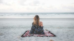 A woman sitting on a blanket on the beach, looking out over the ocean